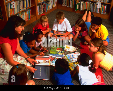 Dix jeunes enfants assis et portant sur le sol dans un cercle comme un adulte enseignant lit à partir d'un livre Banque D'Images