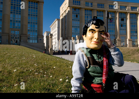 Un gros plan d'un enfant avec masque superman assis sur l'herbe en face de bâtiments modernes à Montpellier, France Banque D'Images