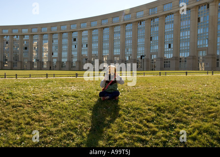 Un gros plan d'un enfant avec masque superman assis sur l'herbe en face de bâtiments modernes à Montpellier, France Banque D'Images