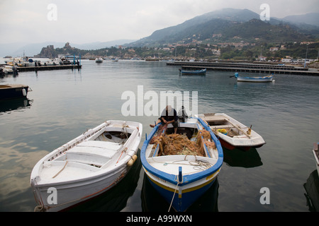 Fisherman mending sicilienne filets à bord de son fishingboat dans l'embarcation de plaisance et le port de Cefalu Sicile Italie Banque D'Images