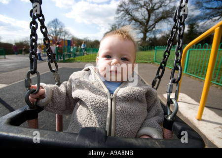 Un petit garçon de 9 mois, joue sur une balançoire du parc England UK Banque D'Images