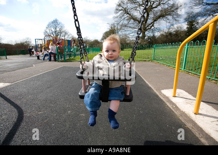 Un petit garçon de 9 mois, joue sur une balançoire du parc England UK Banque D'Images