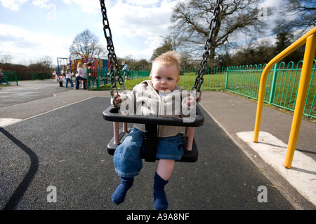 Un petit garçon de 9 mois, joue sur une balançoire du parc England UK Banque D'Images