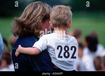 Vue arrière de l'enfant de sexe masculin dans les bras de la mère à l'école primaire nr funrun London UK Banque D'Images