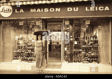 Le noir et blanc d'une jeune femme debout en face de la Maison du Leica Camera shop à Paris sous son parapluie Banque D'Images