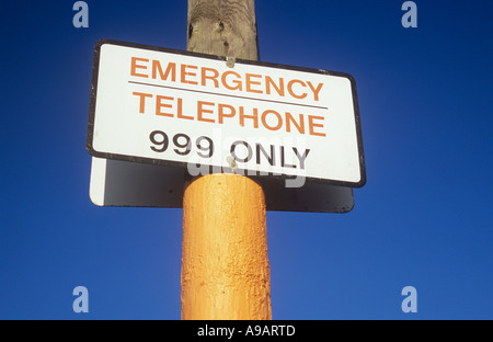 Signe sur un poteau de téléphone orange et marron contre un ciel bleu profond indiquant que 999 de téléphone d'urgence Banque D'Images