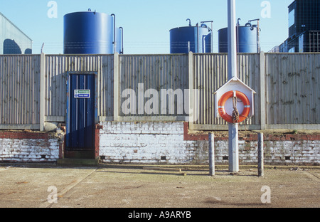 Scène industrielle avec des réservoirs de stockage d'entrepôt chimique bleu mur porte conteneurs clôture lampadaire bouée et ciment road Banque D'Images