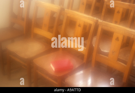 Atmospheric rangées de chaises en bois simple avec un livre rouge couché sur un siège baigné de lumière du soleil d'or Banque D'Images