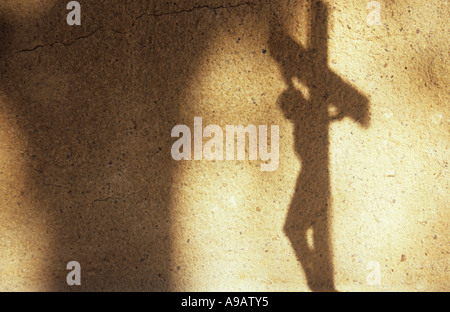 Une ombre contre un mur de rendu pâle Jésus Christ suspendu à un crucifix avec d'autres ombres de pilier et passage voûté Banque D'Images