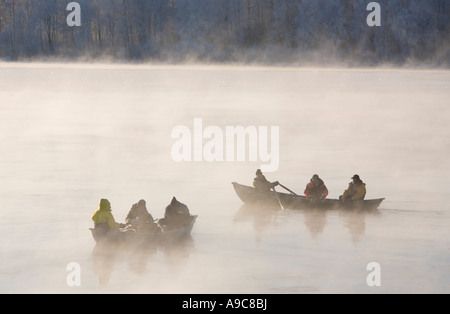 Les pêcheurs jigent des lavarets de barques / skiffs / dinghies à la journée froide d'hiver à la rivière Oulujoki Oulu, en Finlande Banque D'Images