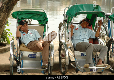 Les pilotes Cyclo une sieste par la rivière Thu Bon à Hoi An, Vietnam central. Banque D'Images