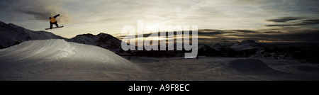 Image panoramique crépuscule de snowboarder Jumping off ramp tour flash grab Banque D'Images