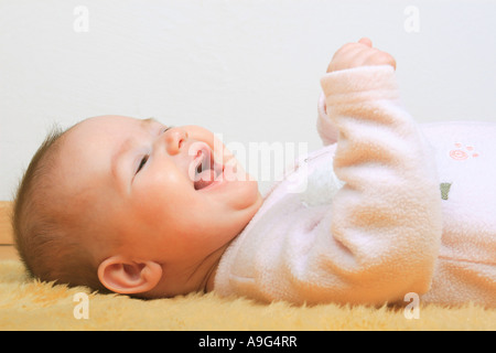 Bébé couché sur le tapis en peau de mouton, rire Banque D'Images