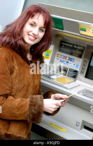 Red-haired woman au distributeur automatique de billets, tenant dans une main. Banque D'Images