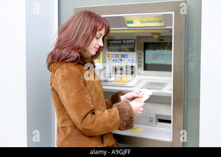 Red-haired woman au distributeur automatique de billets, tenant dans une main. Banque D'Images