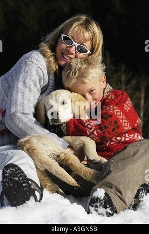 Woman with boy et chiot Golden Retriever couché dans la neige. Banque D'Images