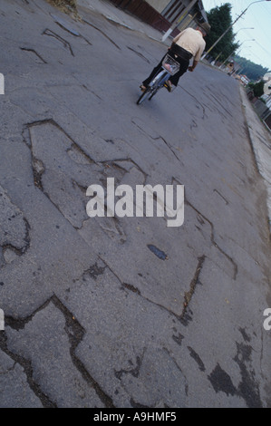 Vieil Homme à vélo sur une route roumaine précaire Banque D'Images