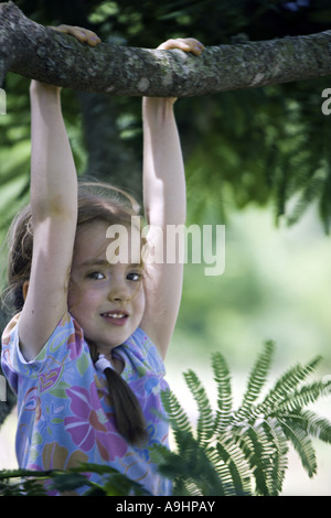 Caroline du Sud YORK belle jeune fille avec des nattes sourire alors qu'elle se bloque par ses mains de la branche d'un arbre mimosa Banque D'Images