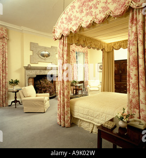 Toile blanche et rose-de-Jouy rideaux sur lit à baldaquin avec des draps crème crème en chambre Banque D'Images