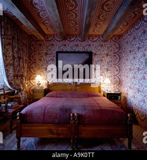 Les lampes allumées de part et d'autre de 2 lits simples avec draps rose foncé en pays chambre avec du papier peint à motifs floraux Banque D'Images