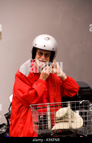 Personnes âgées Bermudes plus vieil homme en manteau de pluie rouge à côté du casque scooter Banque D'Images