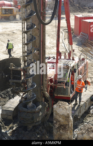 La vis sans fin d'alésage gros plan de Londres est fixée à un grand engin de palplanches à côté d'un tas de béton exposé, avec un travailleur debout sur caterpillar Track England UK Banque D'Images