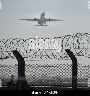 La sécurité de l'aéroport London Heathrow mise au point nette sur le fil du rasoir de dissuasion anti intrus sur périmètre clôtures métalliques jet airliner taking off England UK Banque D'Images