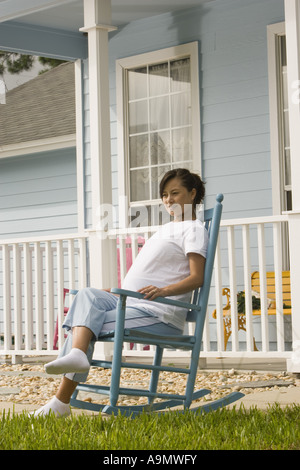 Femme enceinte assise sur un rocking-chair in front of house Banque D'Images