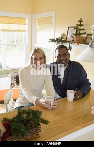 Portrait d'un couple inter-racial avec les tasses à café assis à un comptoir de cuisine Banque D'Images