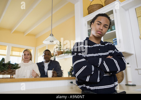 Portrait d'une inter-raciale teenage boy standing dans la cuisine avec les parents dans l'arrière-plan Banque D'Images