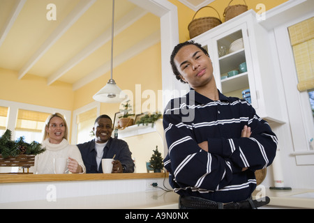 Portrait d'une inter-raciale teenage boy standing dans la cuisine avec les parents dans l'arrière-plan Banque D'Images