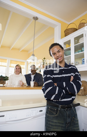 Portrait d'une inter-raciale teenage boy standing dans la cuisine avec les parents dans l'arrière-plan Banque D'Images