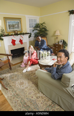 Famille en pyjama assis dans la salle de séjour décorée pour Noël Banque D'Images