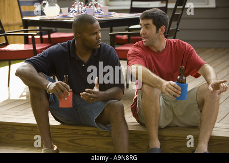 Deux hommes assis sur les marches de backyard patio offrant des boissons froides Banque D'Images