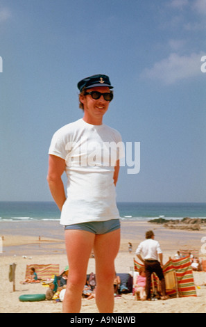 Jeune homme caucasien portant une casquette de marin à pic, un t-shirt blanc et un maillot de bain sur la plage, années 1960 Archiver la photo Banque D'Images