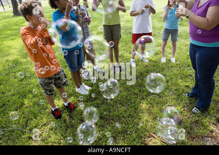 Les enfants et leur enseignant faisant des bulles dans un parc Banque D'Images