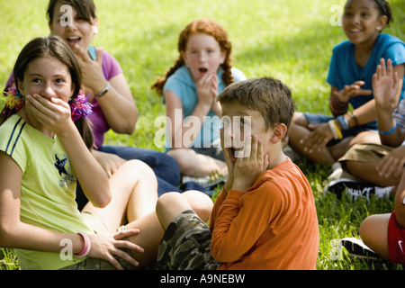 Les enfants et leur enseignant qui surpris visages alors qu'il était assis sur l'herbe dans un parc Banque D'Images