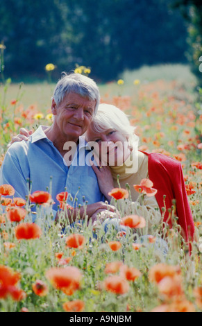 Portrait happy senior couple sitting in champ de coquelicots Banque D'Images