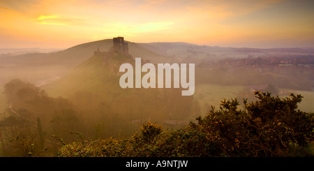 Château de Corfe Castle à l'abandon près de Swanage Dorset avec l'éclairage orangé de l'aube dans le ciel et brouillard tourbillonnant dans la vallée Banque D'Images