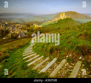 Château à l'abandon et le village de Corfe Castle in early morning light et un ciel clair avec des marches menant vers le bas de la colline Banque D'Images