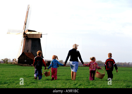 La mère et les enfants avec des paniers traversant les terres agricoles se tenant la main en Hollande près de Windmill Banque D'Images