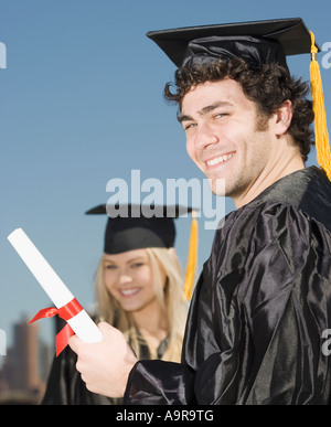 Man wearing graduation cap and gown avec diplôme Banque D'Images