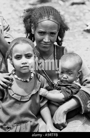 Portrait noir et blanc d'une femme, portant une coiffure et une robe traditionnelles, avec sa fille et son bébé à l'extérieur d'une clinique de santé rurale à Tigray, en Éthiopie Banque D'Images
