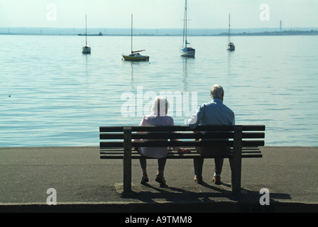 Vue arrière des retraités de cheveux gris mûrs hommes et femmes âgés couple assis sur une banquette en bord de mer donnant sur la station balnéaire de la Tamise Essex Angleterre Royaume-Uni Banque D'Images