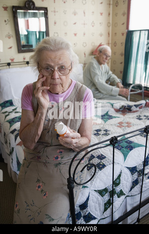 Senior woman sitting on bed looking at prescription bottle Banque D'Images