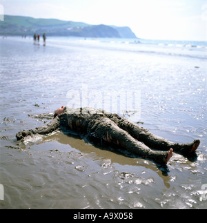 Un homme couché reposant sur le bord de la mer couverte de sable sur la plage de Borth Ceredigion Pays de Galles UK Banque D'Images