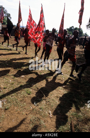 Lolgorian, au Kenya. Massaï Siria ; cérémonie Eunoto ; ligne de Moran qui traversent le Manyatta portant des drapeaux. Banque D'Images