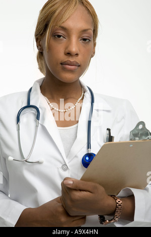 Jeune femme médecin dans un manteau blanc avec un presse-papiers et d'un stéthoscope ressemble au sérieux à l'appareil photo Banque D'Images