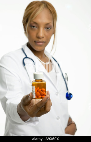 Young female doctor holding une bouteille de pilules à l'appareil photo, la bouteille est dans l'accent Banque D'Images