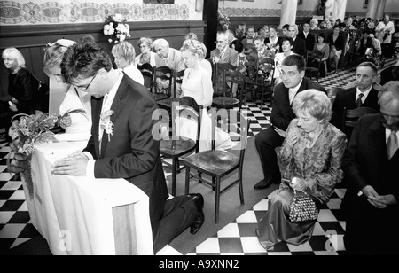 Pologne, Lodz, mariée et le marié avec les invités du mariage à genoux dans l'église (B&W) Banque D'Images